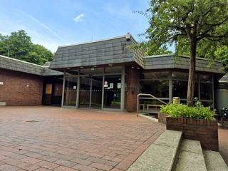 Außenansicht Eingang Hallenbad Barrierefreier Eingang eines backsteingebauten Gebäudes, umgeben von grünen Bäumen.