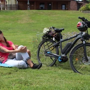 Radfahren in der Mittelweser-Region Eine Frau und ein Mann relaxen auf einer Wiese neben ihrem E-Bike in einer grünen Umgebung.
