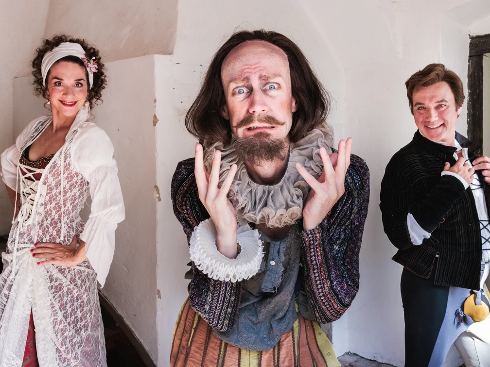 Lerche 1 groß.jpg Drei Schauspieler in historischer Kleidung lächeln lebhaft in einem hellen, beigen Raum.