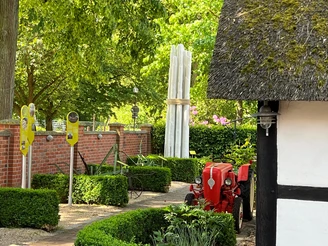 Spargelmuseum Nienburg Ein roter Traktor steht vor dem Eingang eines Museums mit einem hohen Spargelskulptur im Garten.