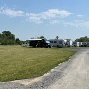 WoMo Weser-Ufer-Urlaub Wohnmobilstellplatz an der Weser mit mehreren Wohnmobilen auf grünem Gras und Schotterweg bei blauem Himmel.