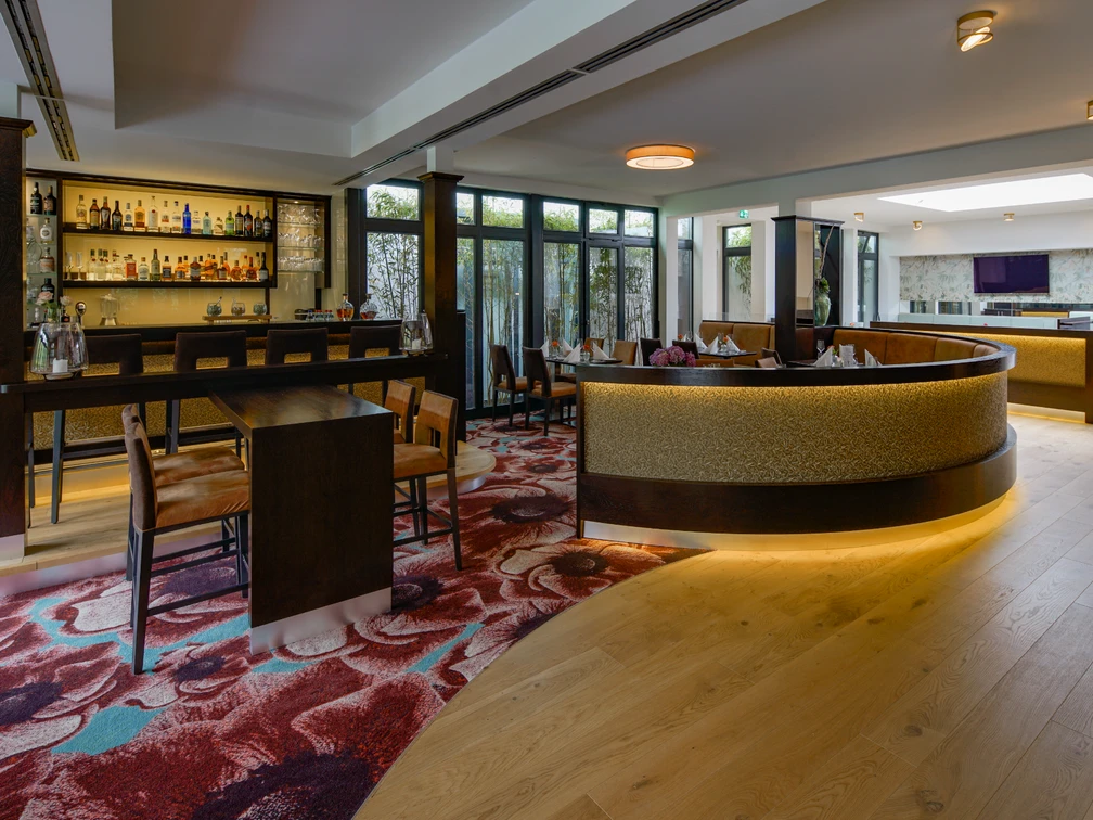 Innenraum im Restaurant merk.Mahl  Moderner Innenraum eines Restaurants mit eleganter Bar, Holzboden und stilvollem Teppichmuster.