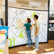 herford-tourist-info-teutoburger-wald-tourismus-h-tornow-001-jpg.jpg Zwei Personen betrachten eine große Karte der Innenstadt von Herford in einer Touristeninformation.