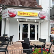 Euphrat.jpg Der Eingang wird vorne mit Tischen und Stühlen zum Sitzen geschmückt und das Logo "Euphrat" in gelb mit einem roten Schriftzug ist vorne direkt über der Tür platziert.