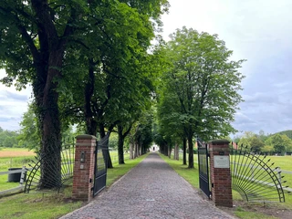 Bild2.jpg Ein idyllischer, von Bäumen gesäumter Weg führt durch ein schmiedeeisernes Tor aus Backstein. Im Hintergrund erstrahlt ein weißes Gebäude und eine wolkenverhangene Atmosphäre rundet das Szenario ab. Die Landschaft vermittelt Ruhe und lädt zum Durchspazieren ein.
