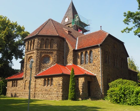 Eine majestätische Kirche aus Sandstein erscheint im Sonnenlicht. Mit rotem Ziegeldach, umgeben von grünem Rasen.