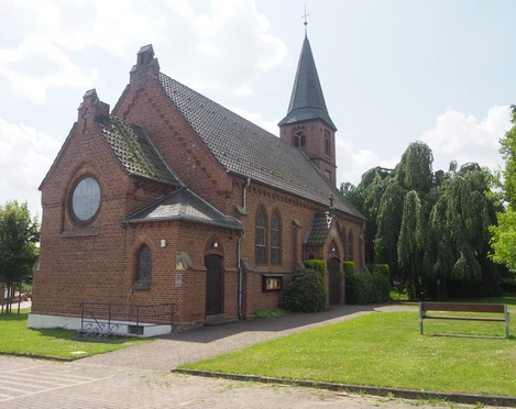 Die Christuskirche Oberbauerschaft ist ein Backsteingebäude mit einem hohen Turm und großen Buntglasfenstern, umgeben von gepflegtem Rasen und Bäumen.
