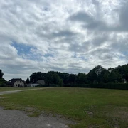 Wohnmobilstellplatz Schützenplatz1.jpg Der Stellplatz liegt unter bewölktem Himmel, von Bäumen umrahmt, mit einem großen Rasenfeld.