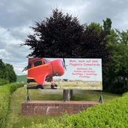 Bild3.jpg Auf dem Bild ist ein Schild am Flugplatz Conneforde zu sehen. Es zeigt ein rotes Flugzeug und wirbt für Rundflüge und Gutscheine der "Fliegerfreunde Conneforde". Umgeben von grünen Hecken steht das Schild vor einem Baum.
