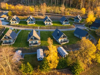 Harz-Urlaubs-Alm in Buntenbock - Luftaufnahme der Ferienhäuser Die Luftaufnahme der Harz-Urlaubs-Alm in Buntenbock zeigt gemütliche Ferienhäuser auf grünen Wiesen, umgeben von bunten Herbstbäumen im Harz.