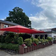 Bild1.jpg Vor einem Restaurant mit dem Banner "Da Mama" stehen rote Sonnenschirme über einer Terrasse mit grünen Pflanzen.