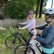 Radfahren in der Mittelweser-Region Zwei Frauen mit Fahrradhelmen pausieren auf E-Bikes neben einem Feldweg, angrenzend an Bäume.