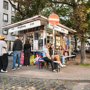 King Georg Kiosk Kleines Kiosk im urbanen Umfeld, umgeben von Bäumen und Menschen in entspannter Atmosphäre.Small kiosk in an urban setting, surrounded by trees and people in a relaxed atmosphere.
