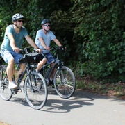Radfahren in der Mittelweser-Region Zwei Männer auf Fahrrädern fahren mit Helmen auf einem asphaltierten Weg, umgeben von Bäumen.