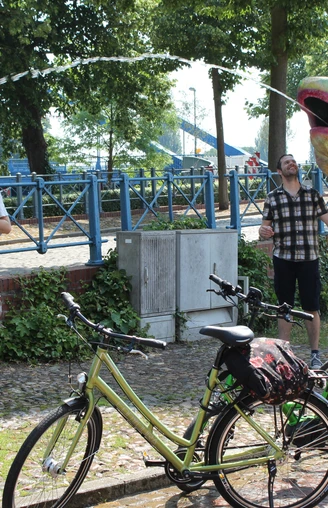 Radfahren in der Mittelweser-Region Menschen genießen einen sonnigen Tag in einem Park, umgeben von Fahrrädern und einer großen, bunten Skulptur.