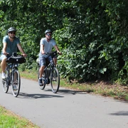 Radfahren in der Mittelweser-Region Zwei Radfahrer auf einem Weg, umgeben von üppigem Grün, genießen eine entspannte Fahrt in der Natur.