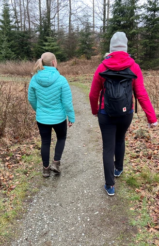 Wandern in der Mittelweser-Region Zwei Menschen in farbigen Jacken und Rucksäcken wandern in einem Waldgebiet auf einem schmalen Pfad.