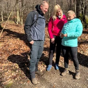 Drei Menschen stehen auf einem herbstlichen Waldweg und betrachten gemeinsam ein Smartphone.