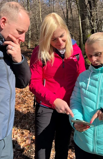 Wandern in der Mittelweser-Region Gruppe wandernd im lichten Laubwald, fokussiert auf ein Smartphone als Wanderhilfe im herbstlichen Umfeld.