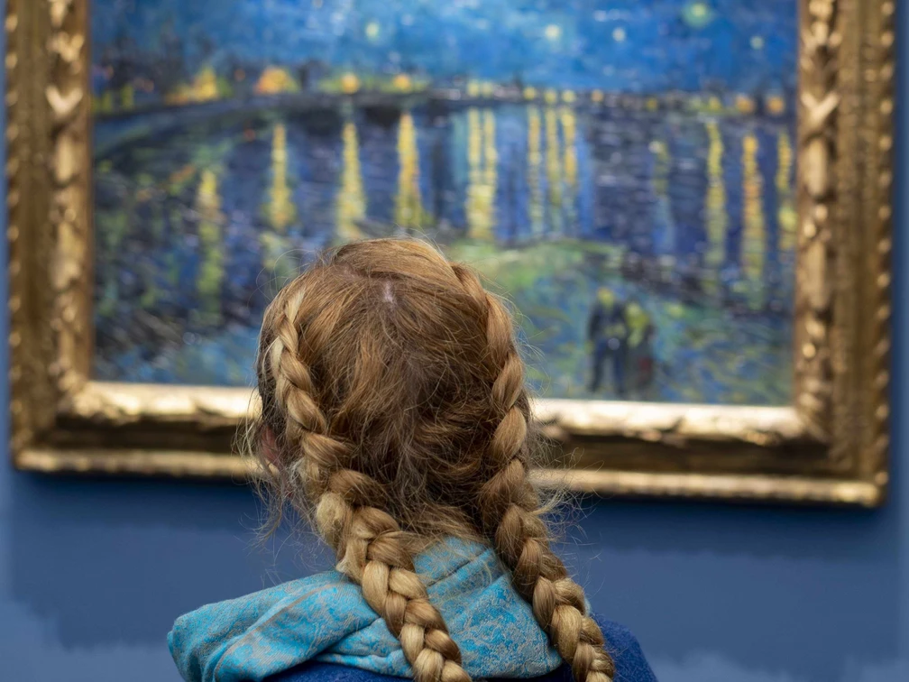 11 Sekunden_Van Gogh (c) Stefan Draschan.jpg Ein Mädchen mit blonden Haaren und einem geflochtenen Zopf steht vor einem blauen Van Gogh Gemälde mir Sternenhimmel.