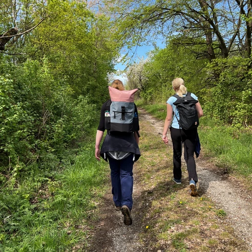 Wandern in der Mittelweser-Region Zwei Wanderinnen mit Rucksäcken auf einem Pfad durch eine grüne, dichte Waldlandschaft.