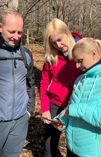 Wandern in der Mittelweser-Region Drei Personen im Wald betrachten eine Karte bei sonnigem Wetter; alle tragen Outdoor-Kleidung.