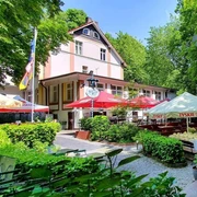 Biergarten in der Schlesischen Schänke im Engelsberger Hof Biergarten der Schlesischen Schänke in Solingen, umgeben von Bäumen, mit bunten Schirmen und Sitzflächen.