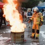 Night of Technology Cologne Ein Feuerwehrmann in vollständiger Ausrüstung steht neben einem brennenden Metallfass.A firefighter in full equipment stands next to a burning metal barrel.