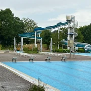 Freizeitbad Münchehagen: Großer Außenbereich mit Wasserrutsche, umgeben von Bäumen und Liegestühlen.