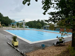 Freizeitbad Münchehagen Ein großes Freibad mit türkisblauem Wasser, umgeben von Bäumen und ausgestattet mit Rutschen.