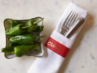 Canito l'acqua - Mediterrane Küche auf Leipzigs Kanälen Grüne Pepperoni in einer Tapas-Schale und ein in eine weiße Stoffserviertte gewickeltes Bestellset