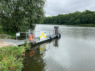 Schiffsanleger Heisterholz Schiffsanleger Heisterholz an einem ruhigen Fluss, umgeben von Wald und Wasser, mit Rettungsring ausgestattet.