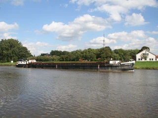 Weser bei Nienburg Ein großer Frachter fährt auf einem ruhigen Fluss nahe Nienburg, umgeben von grünen Bäumen und einem klaren Himmel.