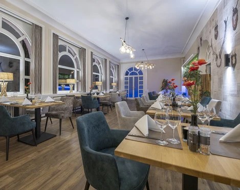 Gastraum im Restaurant Blattwerk im Fletcher Hotel-Restaurant Waldhotel Nordrhein-Westfalen Gastraum im Restaurant Blattwerk mit gedeckten Tischen, grün-blauen Stühlen und großen Fenstern.