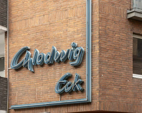 Chlodwig Eck Neonschriftzug "Chlodwig Eck" an einem Backsteingebäude, leicht verwittert, darunter das Eingangsschild.Neon lettering "Chlodwig Eck" on a brick building, slightly weathered, with the entrance sign underneath.