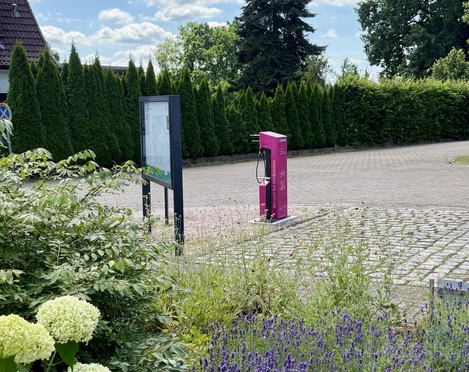 fahrrad-service-station-bispingen-touristik.jpg Eine Fahrrad-Service-Station steht auf einem gepflasterten Platz neben Schildern und grünen Hecken.