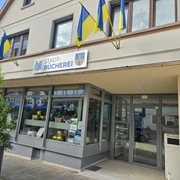 Bad Driburg_Stadtbücherei.jpeg Stadtbücherei Bad Driburg mit gelb-blauen Fahnen, moderner Eingang und klaren Fensterfronten.