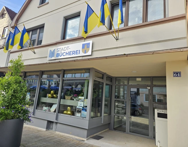 Bad Driburg_Stadtbücherei.jpeg Stadtbücherei Bad Driburg mit gelb-blauen Fahnen, moderner Eingang und klaren Fensterfronten.