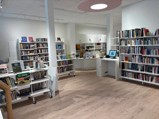 Bad Driburg_Stadtbücherei-3_busch.jpg Innenaufnahme einer modernen Stadtbücherei mit hellen Regalen voller Bücher und einem Empfangstresen.