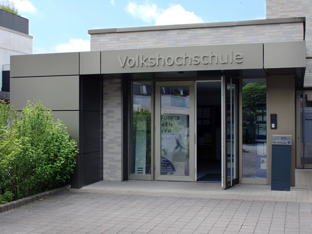 Eingang-Sommer-2025.jpg Moderner Eingang einer Volkshochschule mit barrierefreien Zugangsrampen und automatischen Türen.