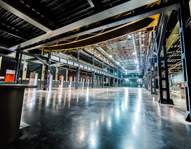 Palladium Köln Haupthalle Die Haupthalle des Palladiums in Köln präsentiert sich als beeindruckende, weitläufige industrielle Veranstaltungsfläche mit glänzendem Boden und einer hohen Stahlkonstruktion, die offene Sicht auf die Dachstruktur bietet.The main hall of the Palladium in Cologne presents itself as an impressive, expansive industrial event space with a gleaming floor and a high steel structure that offers open views of the roof structure.