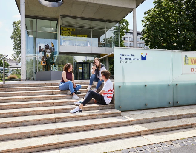 Drei Jugendliche sitzen entspannt auf den Treppen vor dem modernen Eingangsgebäude des Museums für Kommunikation Frankfurt. Drei Jugendliche sitzen entspannt auf den Treppen vor dem modernen Eingangsgebäude des Museums für Kommunikation Frankfurt.Three young people sitting relaxed on the stairs in front of the modern entrance building of the Museum of Communication Frankfurt.
