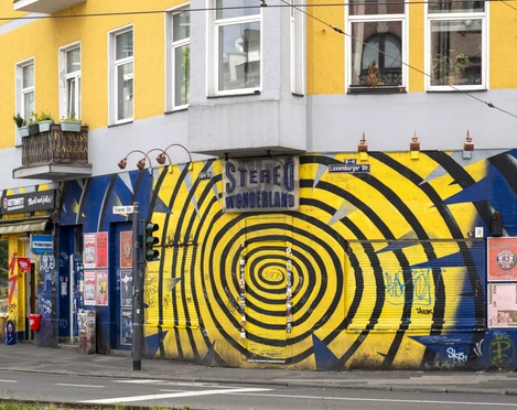 Stereo Wonderland Bunte Graffiti mit Spiralmotiv ziert eine Hauswand, belebt von urbanen Aufklebern und Plakaten.Colorful graffiti with a spiral motif adorns a house wall, enlivened by urban stickers and posters.