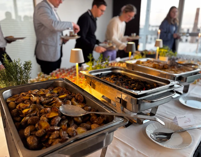 Business Buffet Catering Köln Reihe von Personen bedient sich an einem Buffet mit verschiedenen warmen und kalten Speisen.A row of people help themselves to a buffet with various hot and cold dishes.