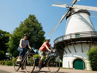 Windmühle in Glandorf Zwei Radfahrer vor einer historischen Windmühle bei sonnigem Wetter.