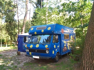 Schaalsee-Camp Wohnmobil umgeben von Bäumen auf einem Campingplatz, blau mit gelben Smileys und Sternen bemalt.