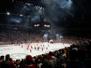 Kölner Haie In einer vollen Eishalle jubeln zahlreiche Fans den Kölner Haien auf dem Eis zu, während dynamische Licht- und Nebeleffekte die Atmosphäre verstärken.In a packed ice rink, numerous fans cheer on the Cologne Sharks on the ice, while dynamic lighting and fog effects enhance the atmosphere.