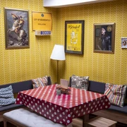 The Bär Das Bild zeigt einen Raum mit gelben Tapeten, einer Sitzecke mit Polsterkissen und dekorativen Bildern an der Wand. Ein Tisch mit rotem Punktetuch steht zentral, ergänzt durch bequeme Holzstühle.The picture shows a room with yellow wallpaper, a seating area with upholstered cushions and decorative pictures on the wall. A table with a red polka dot cloth stands in the center, complemented by comfortable wooden chairs.