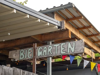 Bumann & Sohn Das Bild zeigt ein Schild mit der Aufschrift "Biergarten", das von bunten Wimpeln umrahmt wird.The picture shows a sign with the inscription "Biergarten" (beer garden) framed by colorful pennants.