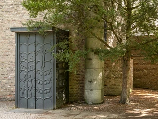 St. Alban Eine moderne Gebäudefassade mit filigranem Metallelement und Schatten eines großen Nadelbaums.A modern building façade with a filigree metal element and the shade of a large conifer.